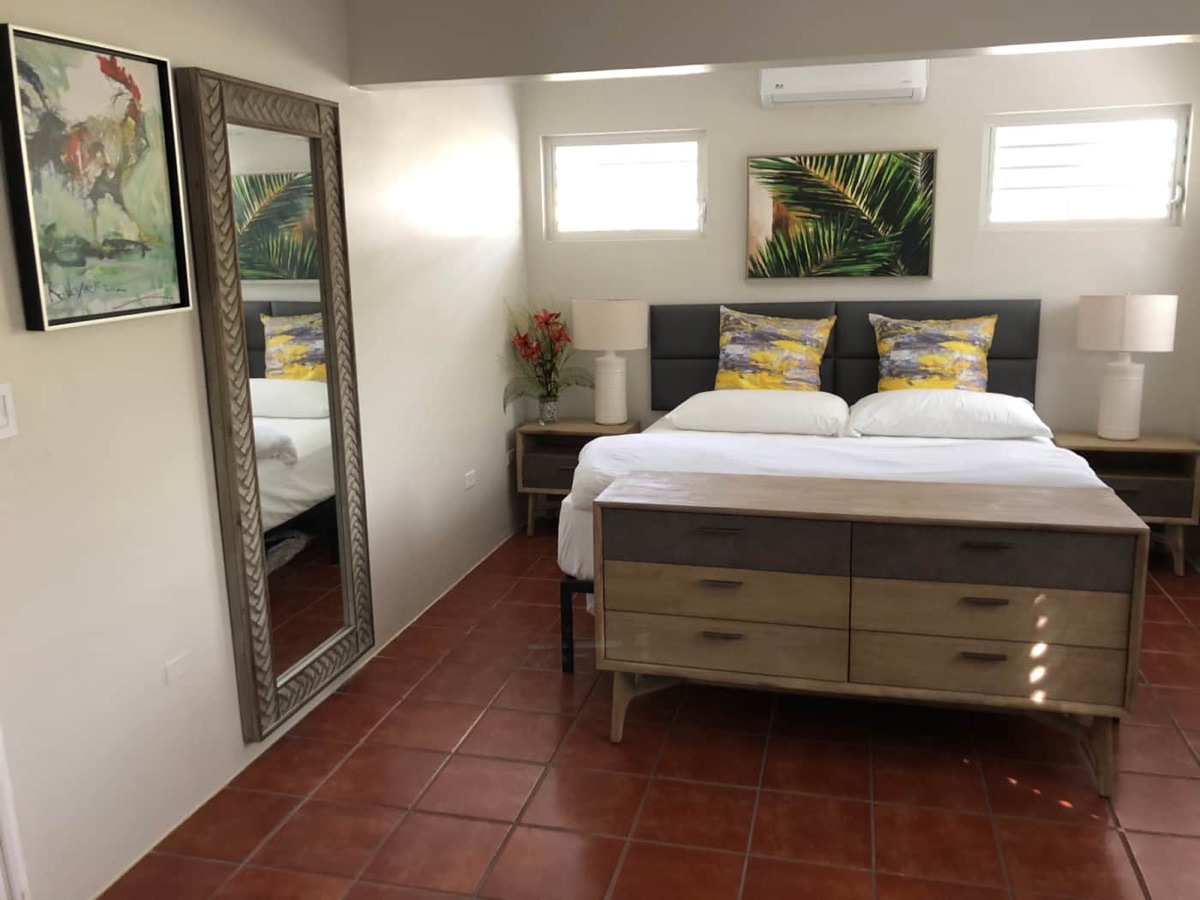 Bedroom with a large bed, dual nightstand lamps, dresser and tropical palm artwork