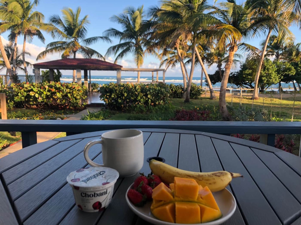 Breakfast of fruit, yogurt and coffee on the patio table overlooking the gazebo, palms and sea