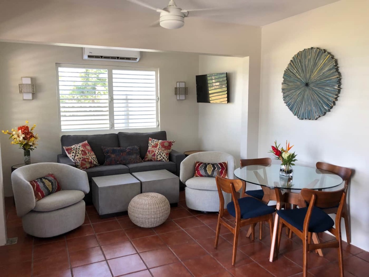 Open living and dining area with sofa, swivel chairs, glass dining table and island artwork